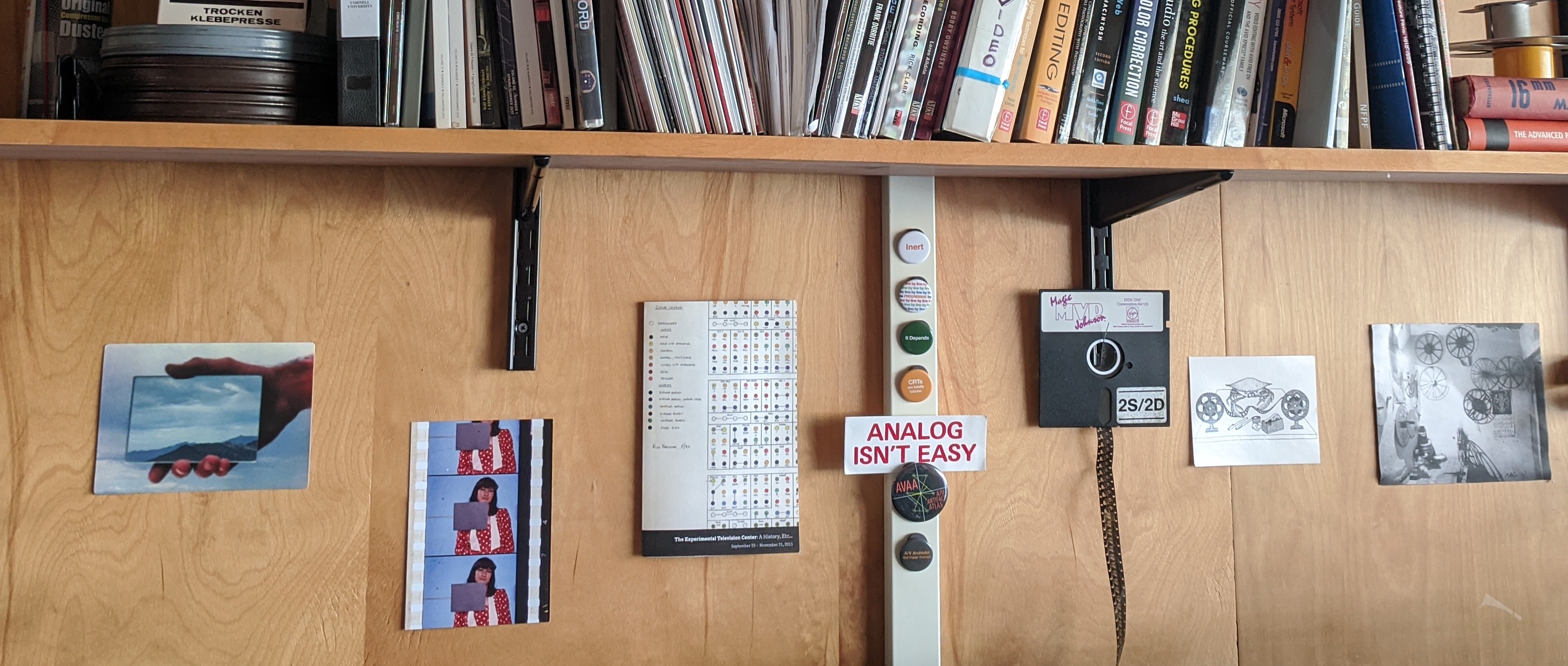 A photograph of wall with objects attached to it, including strips of film and a floppy disk